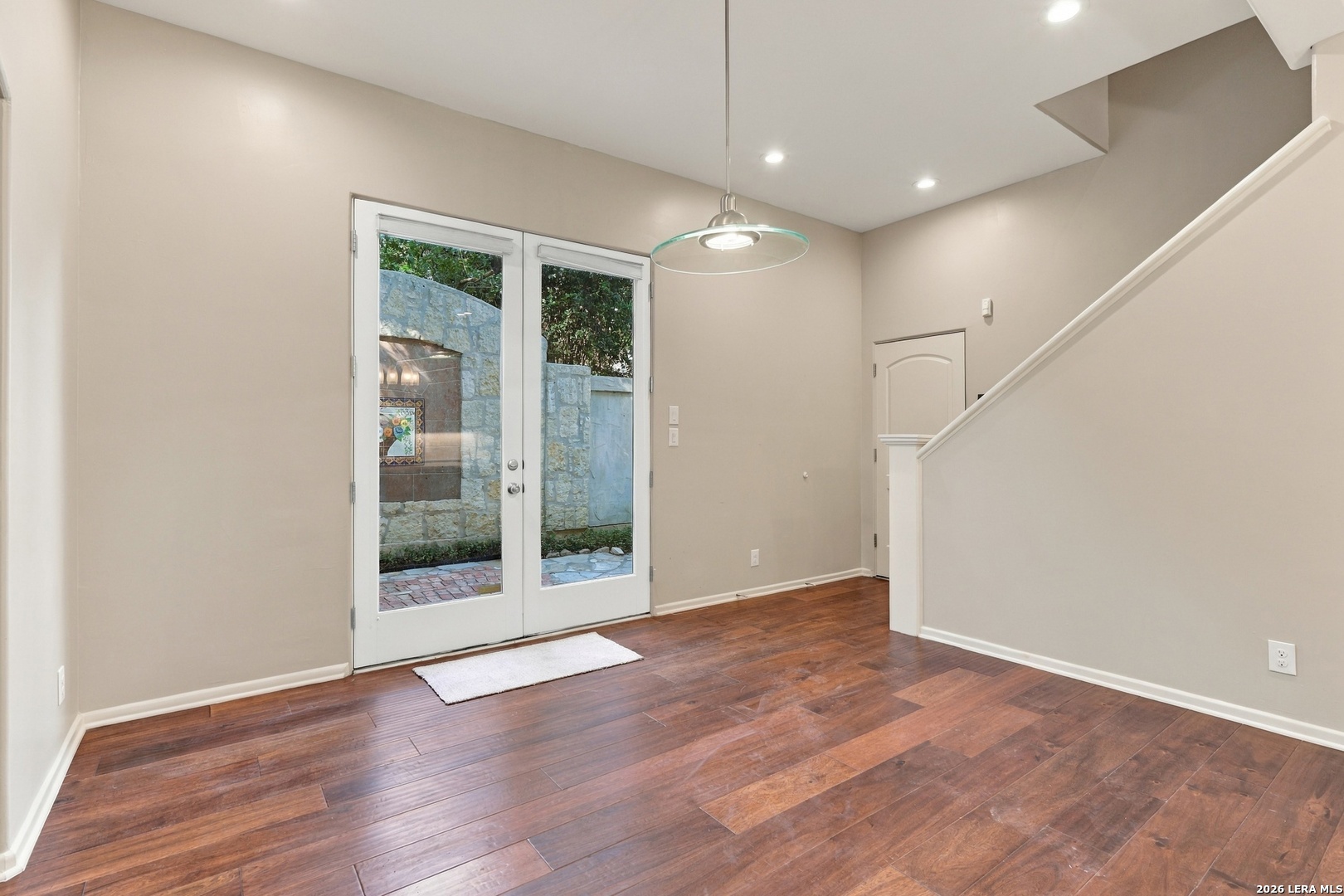 Entry area with hardwood floors, a staircase, and French doors opening to a stone-walled patio.
