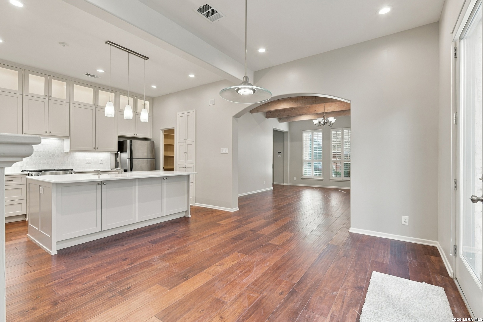 Kitchen and dining area with white cabinetry, a large island, dark wood floors, and exposed ceiling beams.