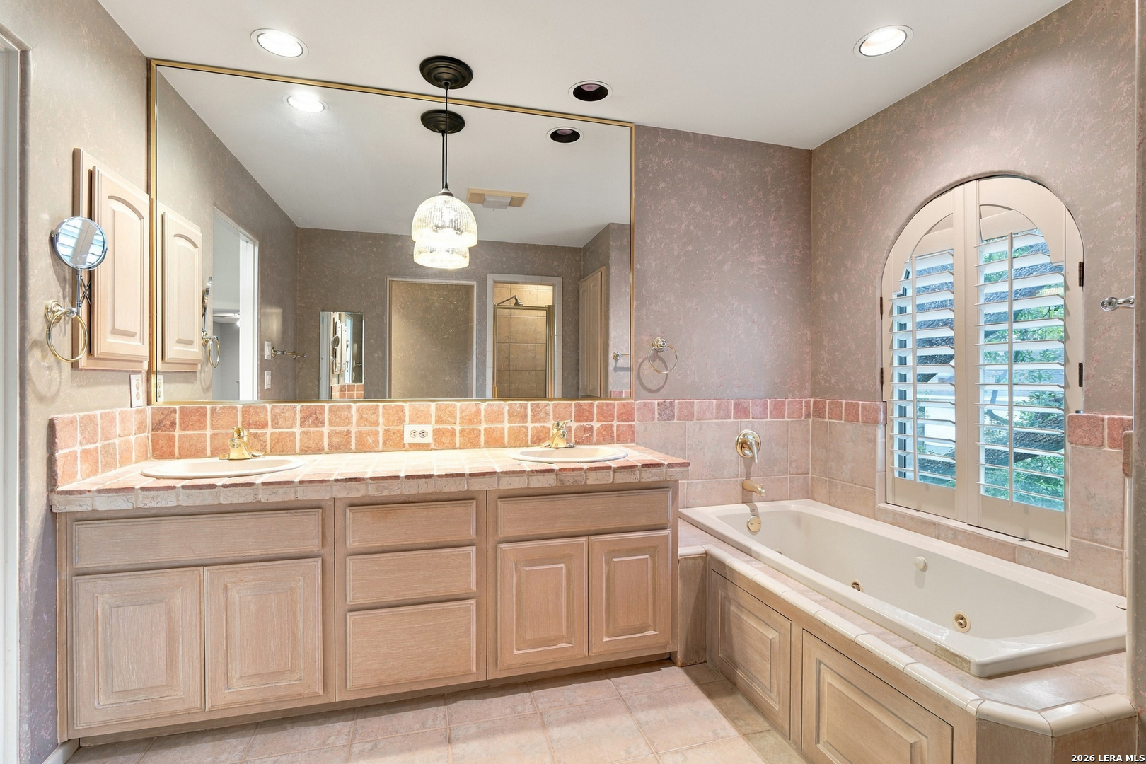 Bathroom with a double vanity, built-in tub, and arched shuttered window.