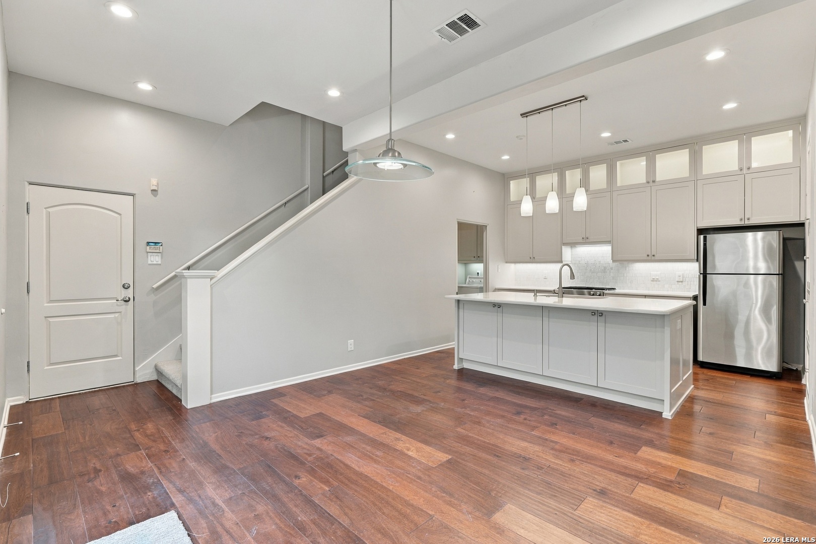 Open-plan kitchen with a large island, stainless steel refrigerator, dark wood floors, and a staircase.