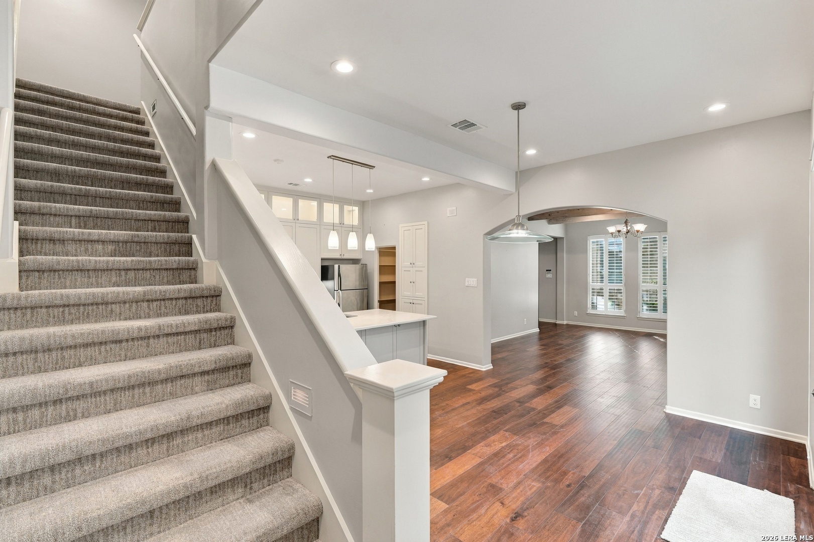Open-plan kitchen and living area with dark wood floors beside a carpeted staircase.