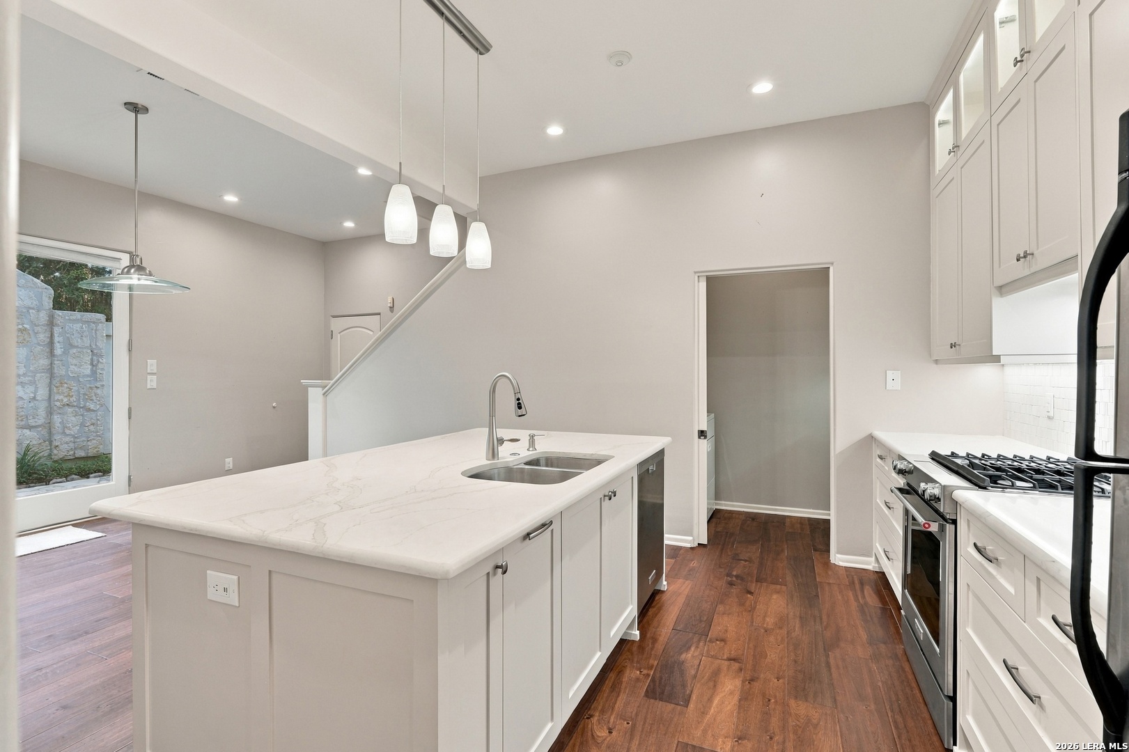 Kitchen with a large quartz island, white cabinetry, stainless steel appliances, and dark wood floors.