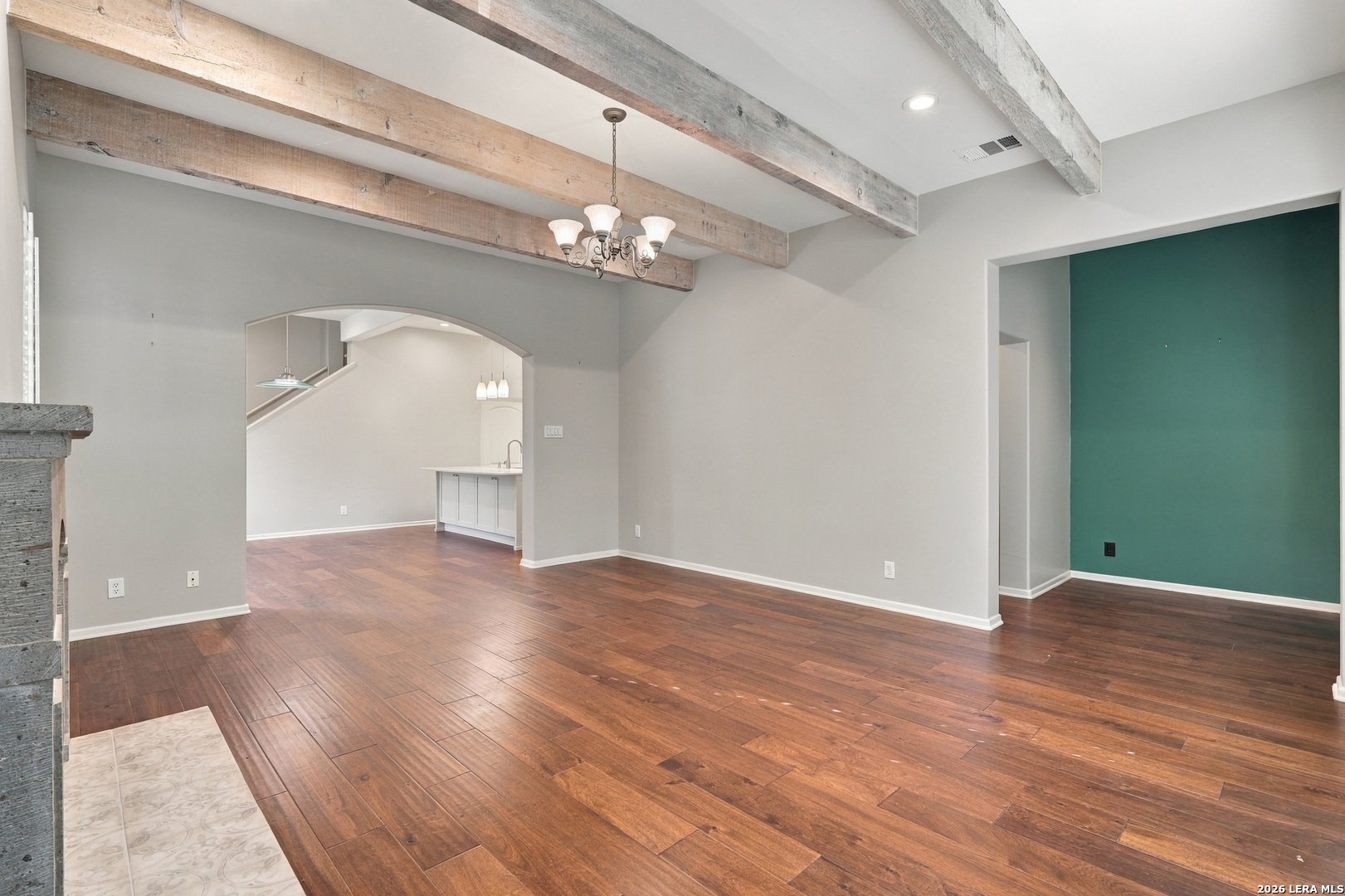 Empty living room with exposed wood beams, hardwood floors, and a teal accent wall.