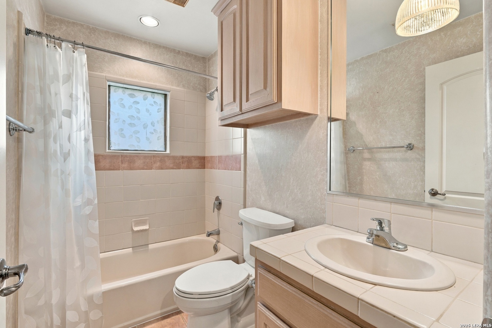 Bathroom with a bathtub, leaf-patterned shower curtain, tiled vanity, and mirrored medicine cabinet.