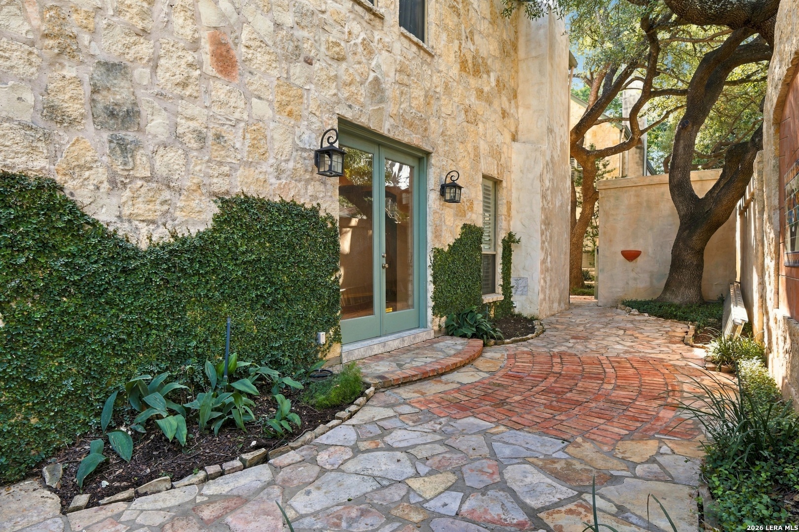 Stone house entrance with a pale green door, ivy-covered walls, and a curved brick-and-flagstone walkway.