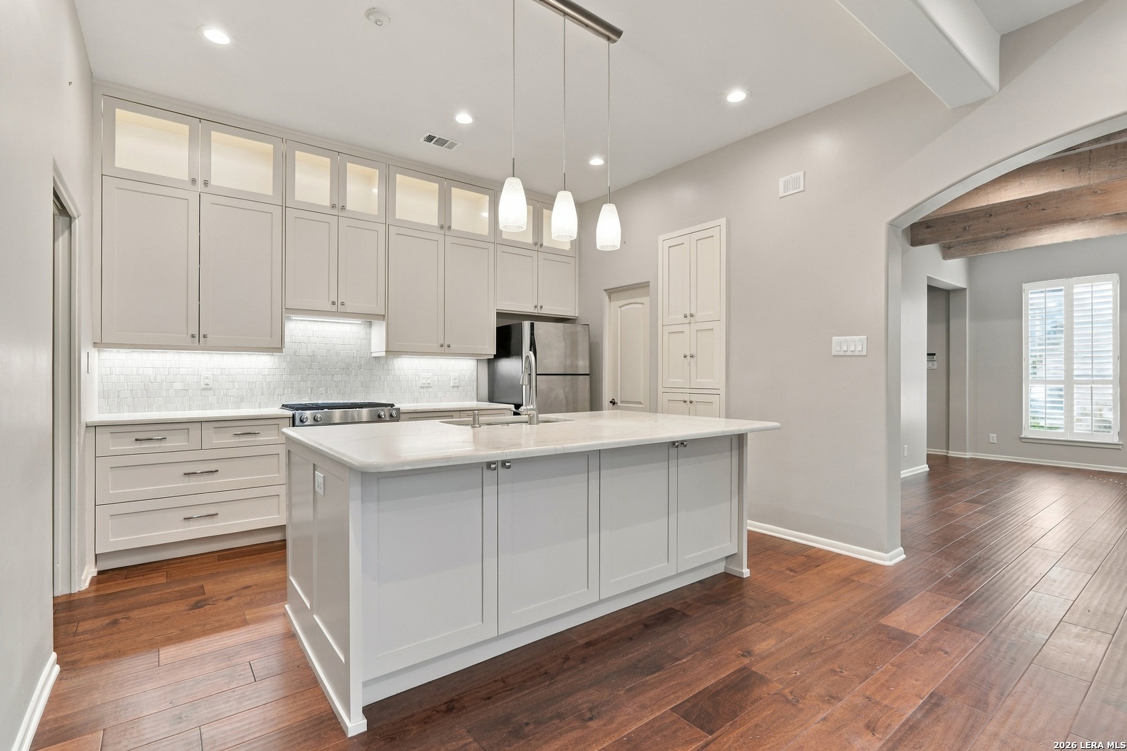 Kitchen with a large white island, tall cabinets, stainless steel appliances, and dark wood floors.