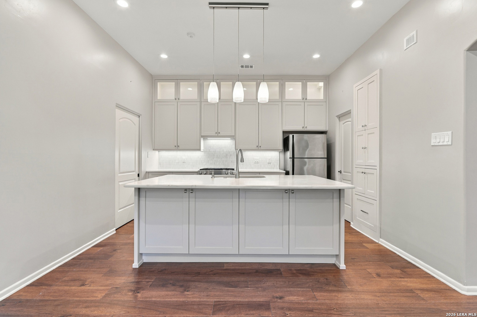 Kitchen with a large white island, ceiling-height cabinets, stainless steel refrigerator, and dark wood floors.