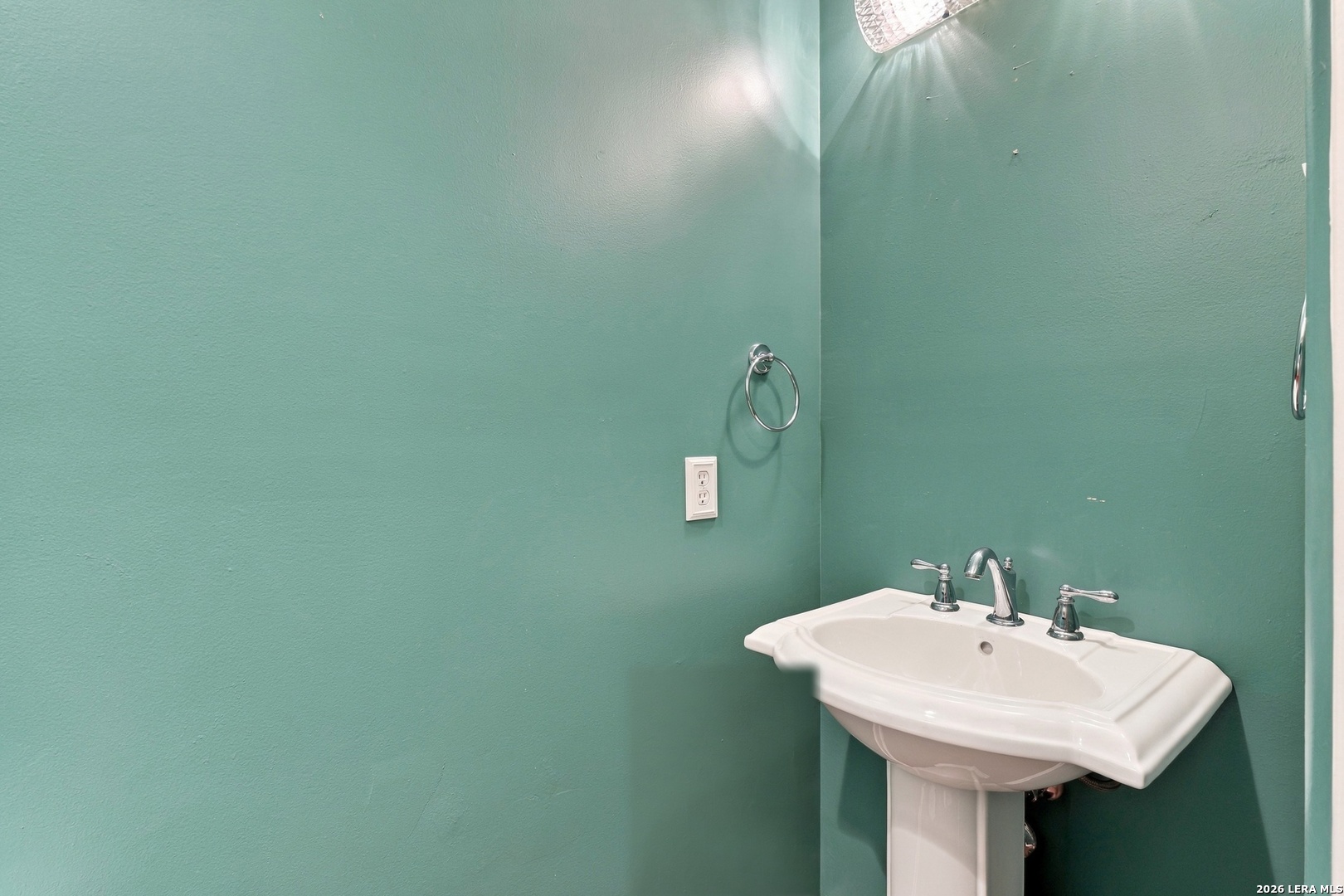 White pedestal sink with chrome fixtures against teal bathroom walls.