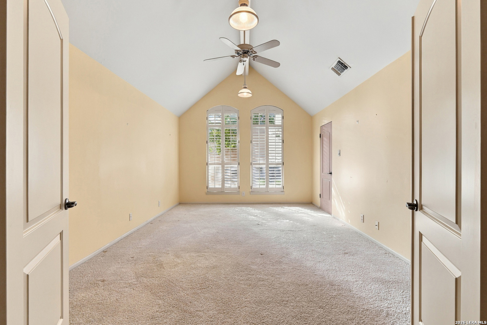 Vacant bedroom with a vaulted ceiling, ceiling fan, and arched shuttered windows.