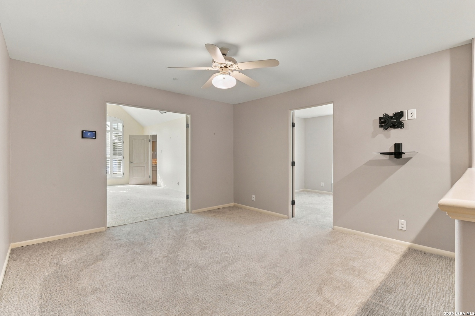 Unfurnished carpeted room with a ceiling fan, TV mount, and open doorways to adjoining rooms.