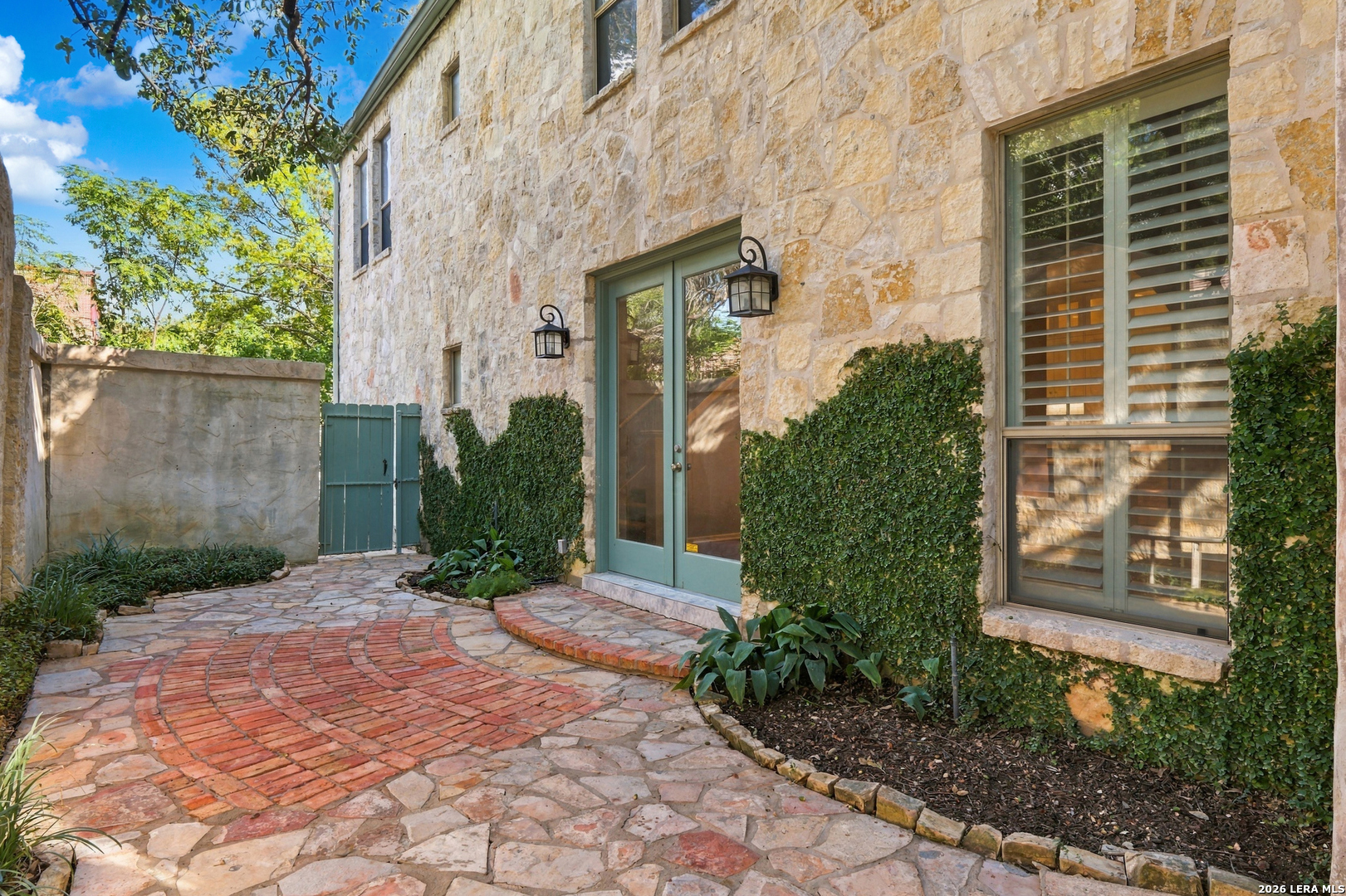 Stone home exterior with ivy-covered walls and a curved brick-and-flagstone courtyard path.