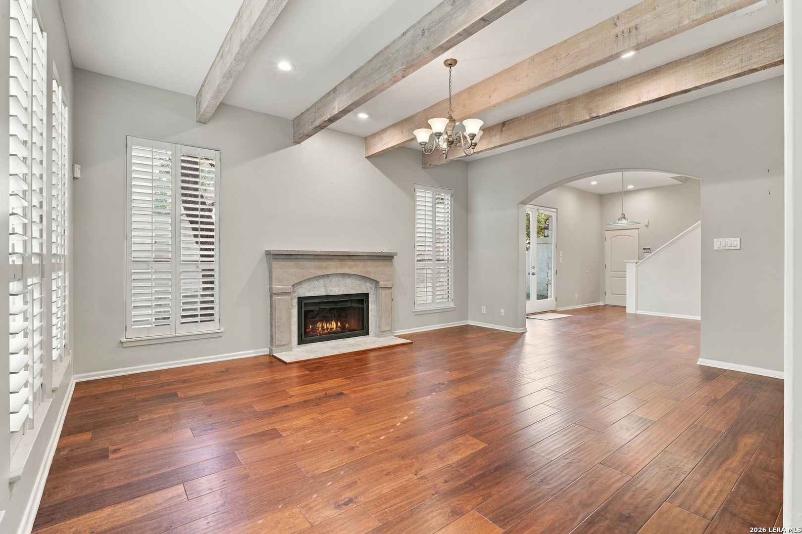 Living room with a stone fireplace, exposed wood beams, and hardwood floors.