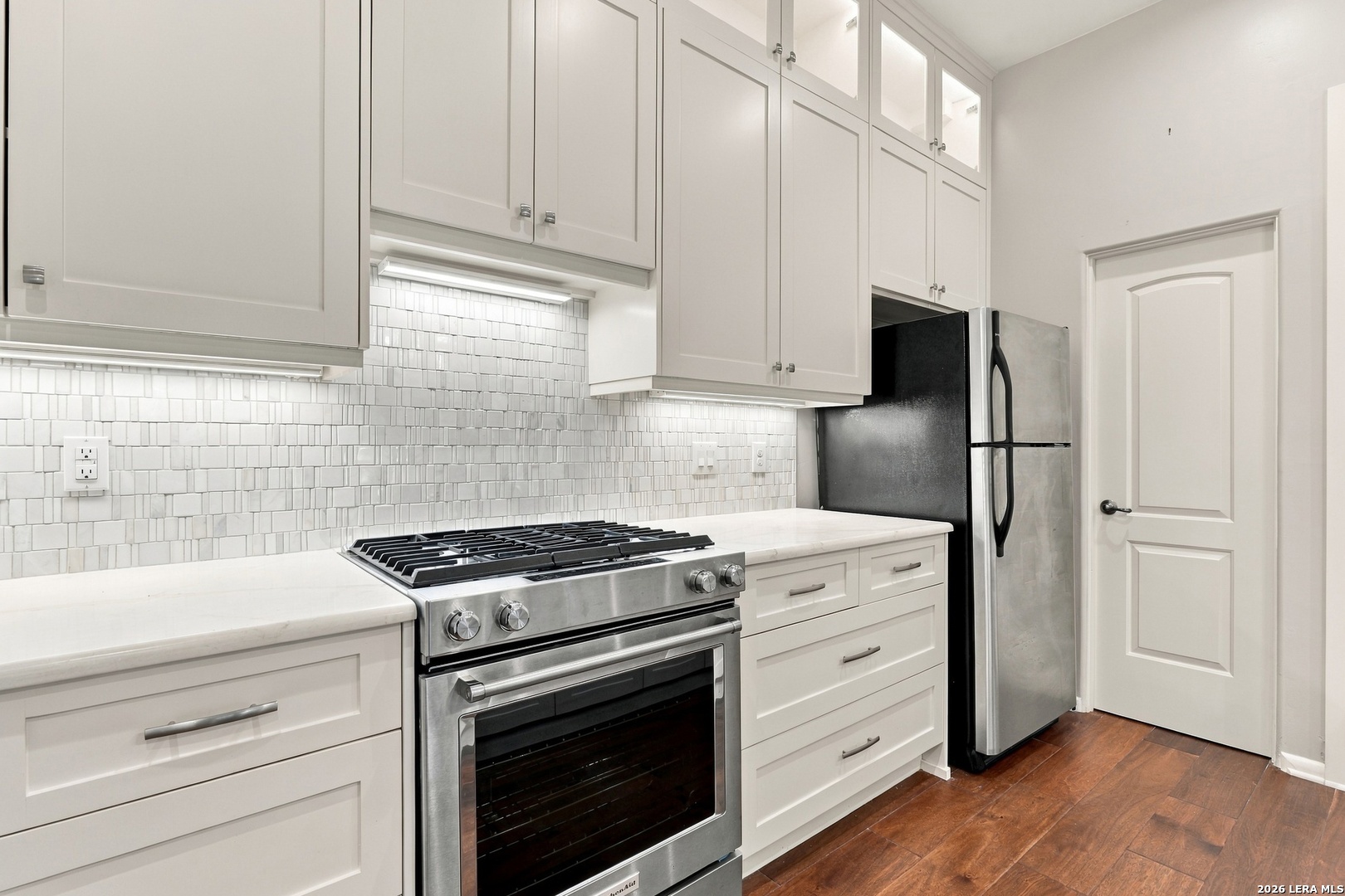 Bright kitchen with white shaker cabinets, a stainless steel gas range, and warm wood floors.