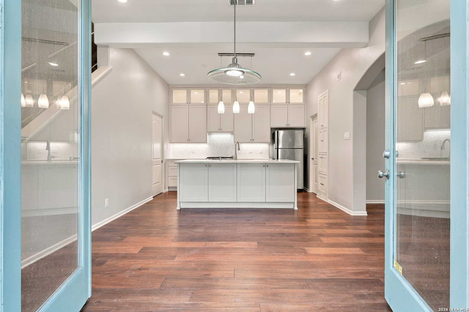 Kitchen with a white island and cabinetry, stainless steel refrigerator, and dark wood floors.