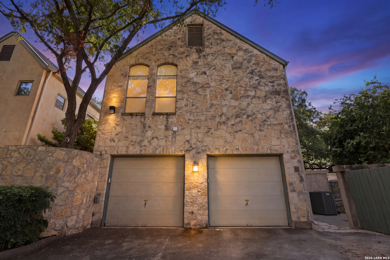 Stone-front house with two garage doors beneath arched windows at dusk.