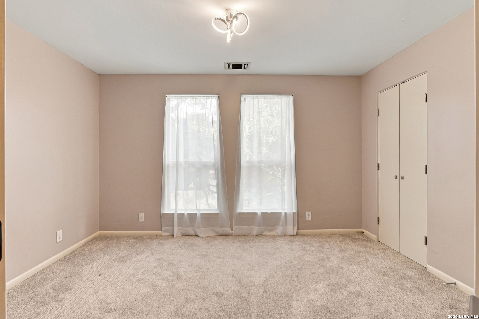 Empty carpeted bedroom with two curtained windows and a double-door closet.