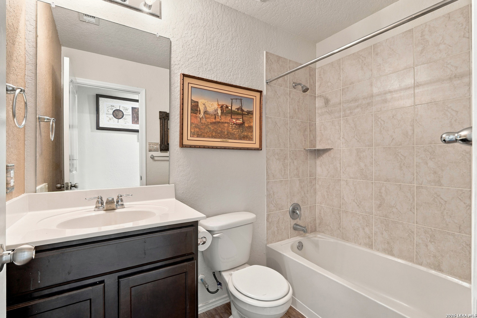 Bathroom with dark wood vanity, white sink and toilet, and a bathtub with beige tile surround.