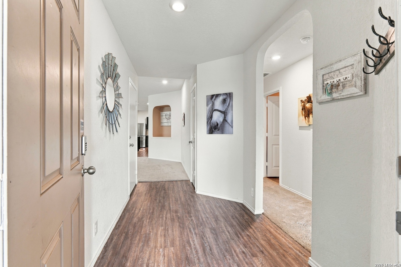 Hallway with wood-look flooring, an arched opening, and horse-themed wall art.