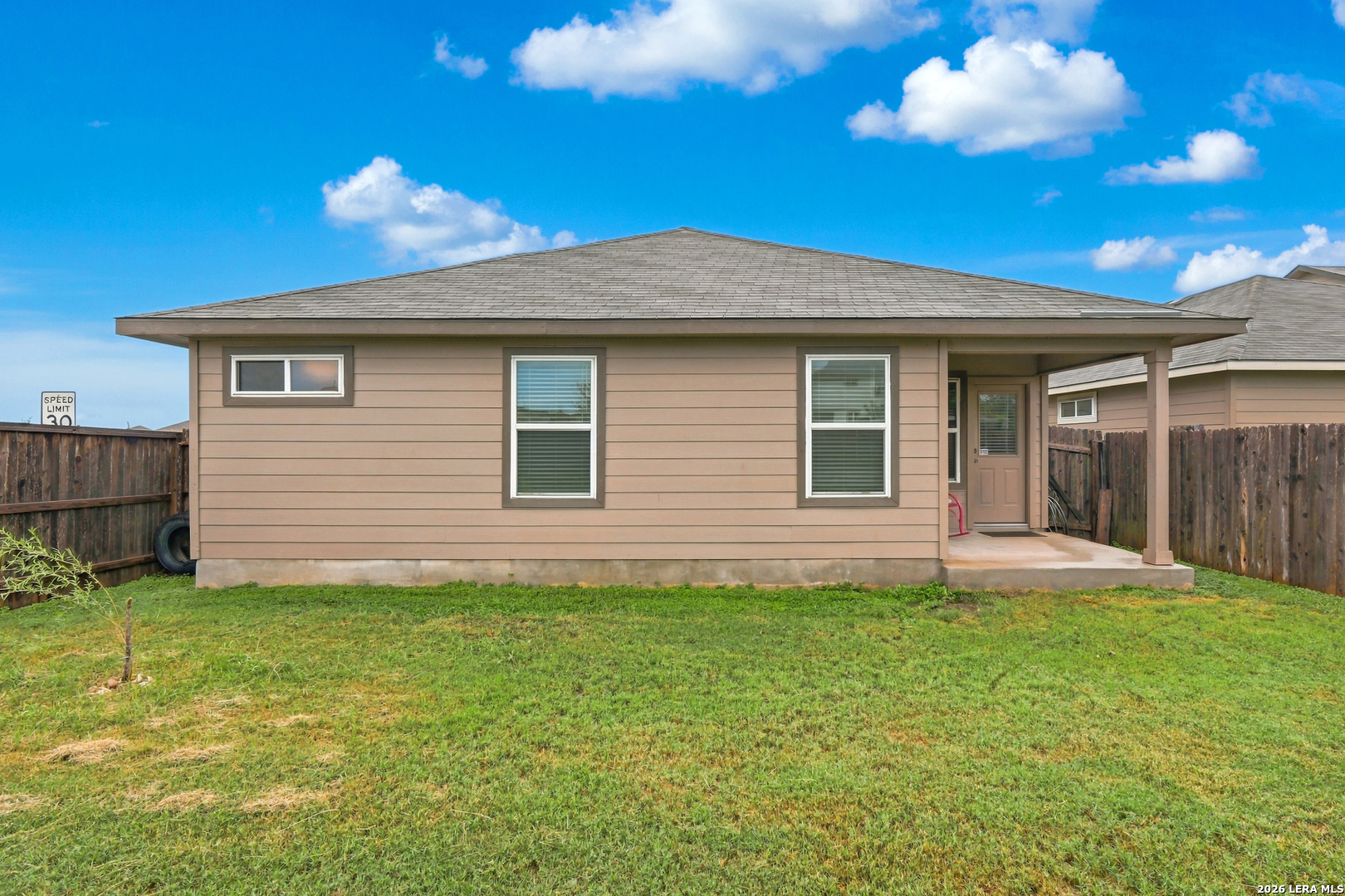 Rear of a tan single-story house with a covered patio and fenced grassy yard.