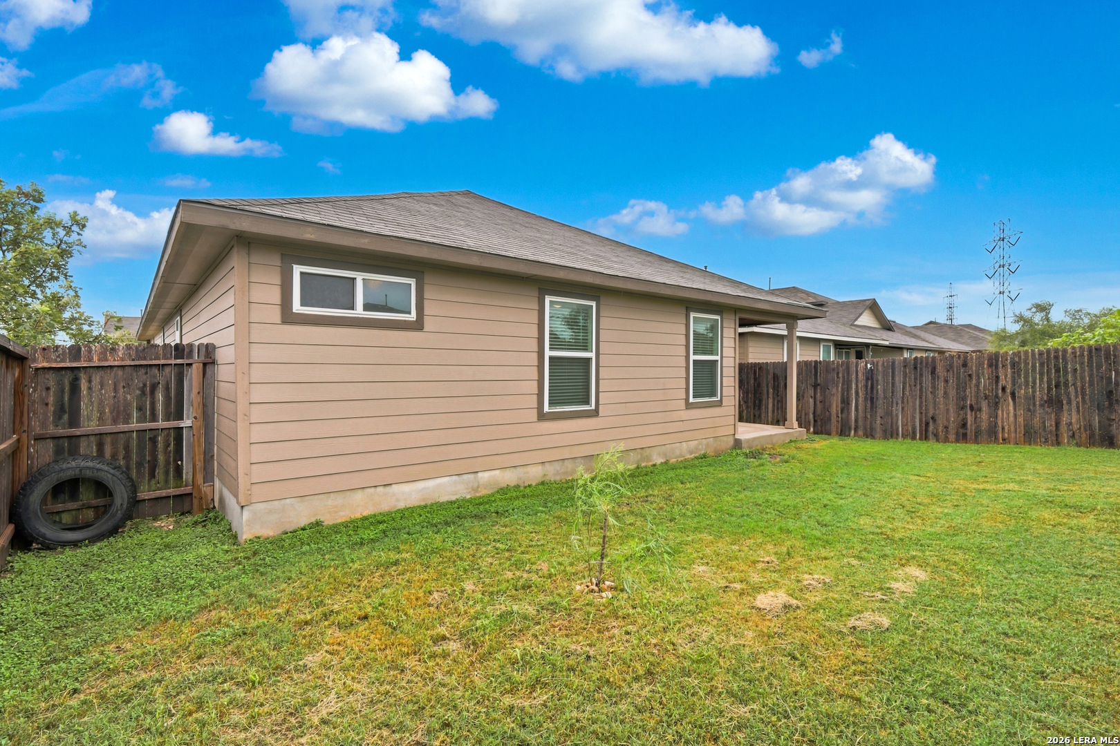 Tan single-story home beside a grassy yard with a wooden privacy fence and small covered patio.