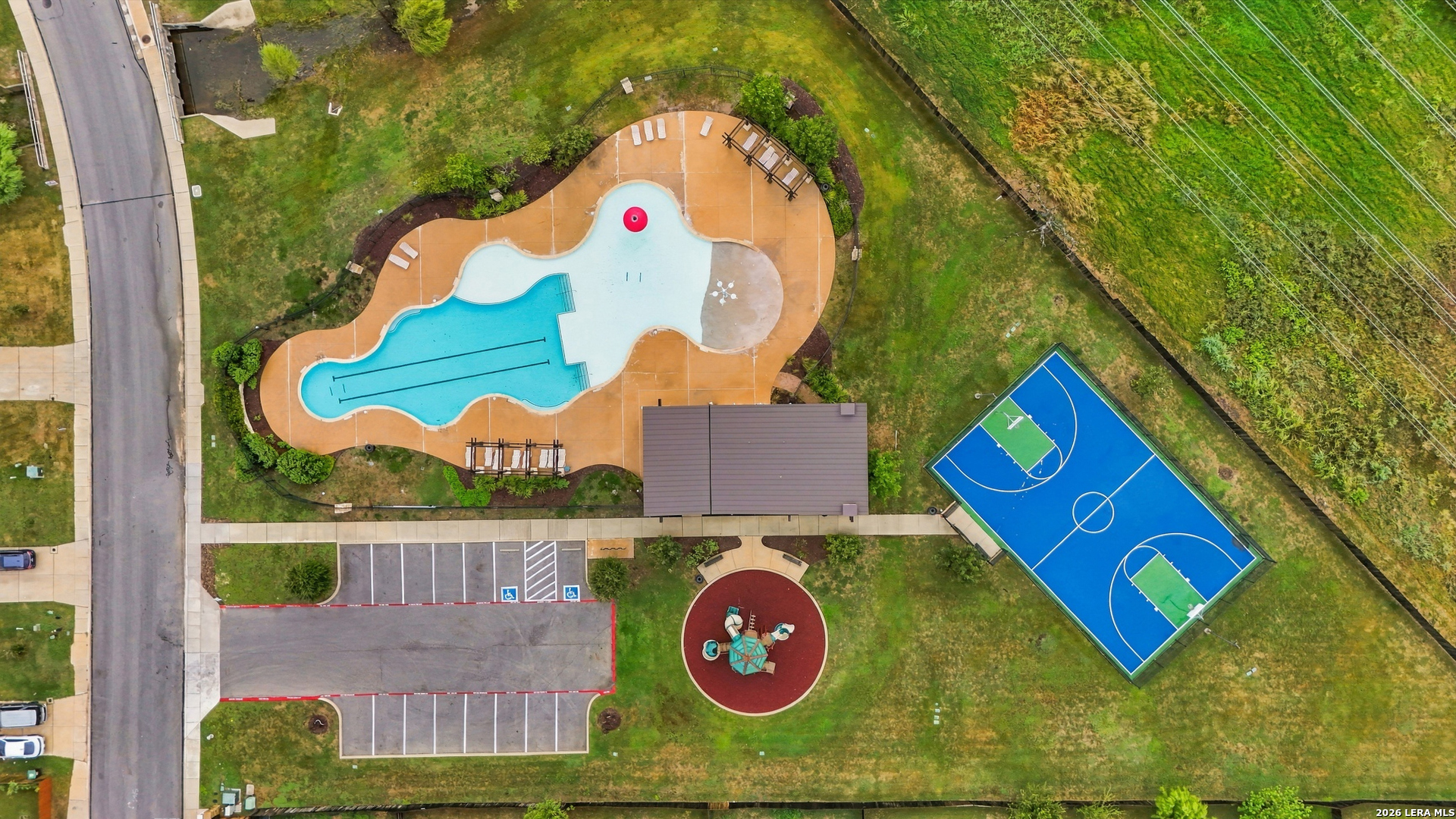 Aerial view of a community pool, basketball court, playground, and parking area.