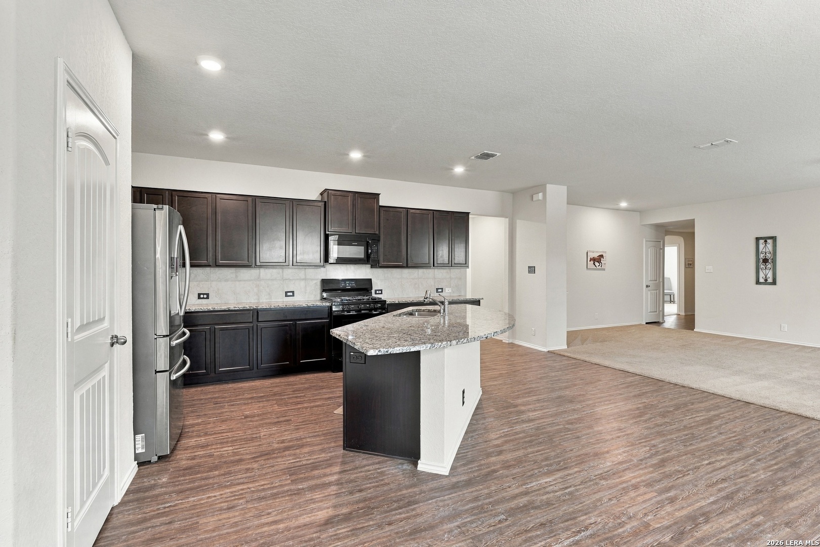 Kitchen with dark cabinets, stainless steel appliances, and a granite island opening to the living area.