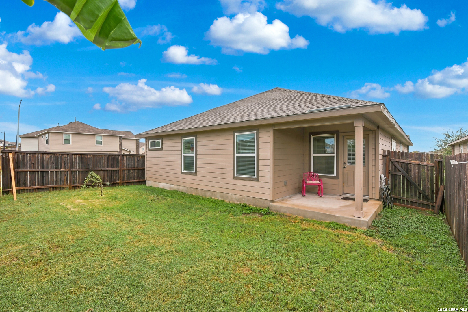 Rear of a tan house with a covered patio and fenced grassy backyard.