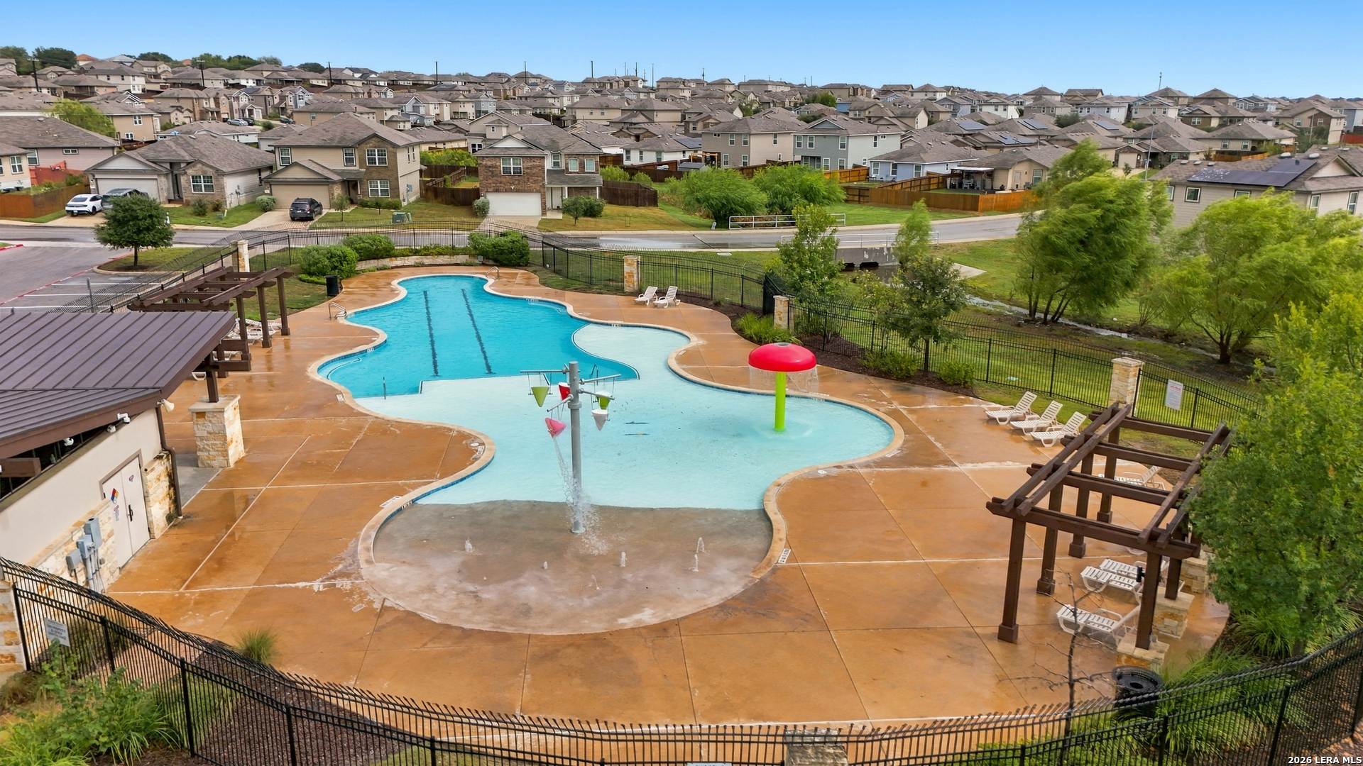 Neighborhood pool with a shallow splash area, mushroom fountain, pergolas, and lounge chairs.