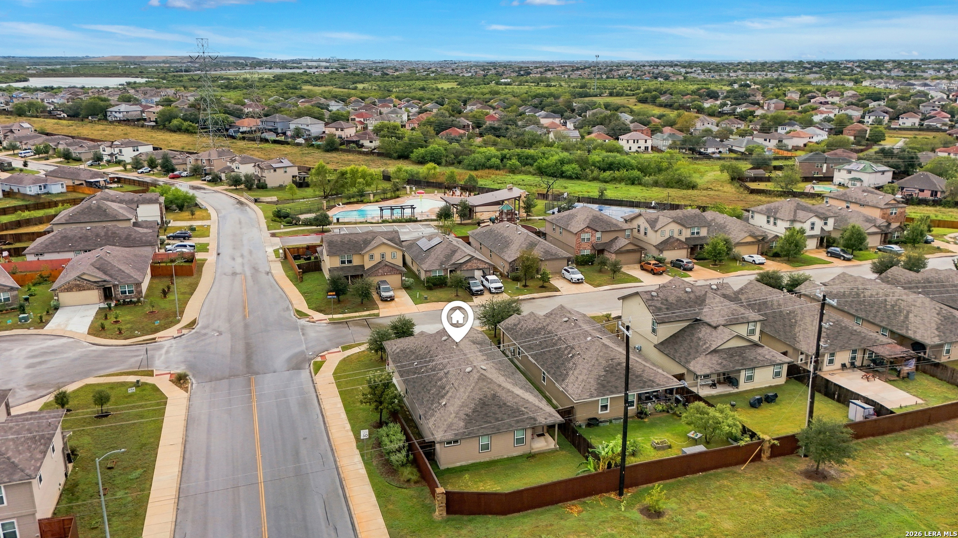 Aerial view of a home in a residential neighborhood, with a community pool visible in the distance.
