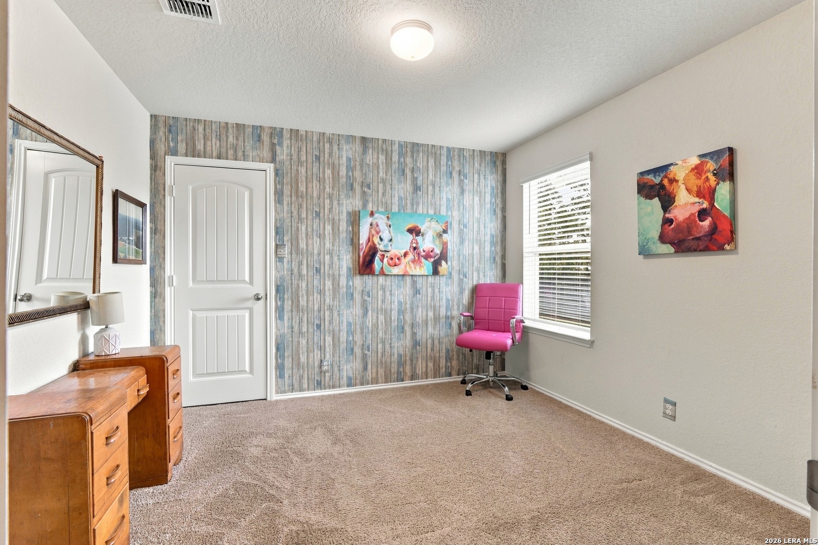 Furnished room with a blue wood-look accent wall, pink office chair, and animal artwork.