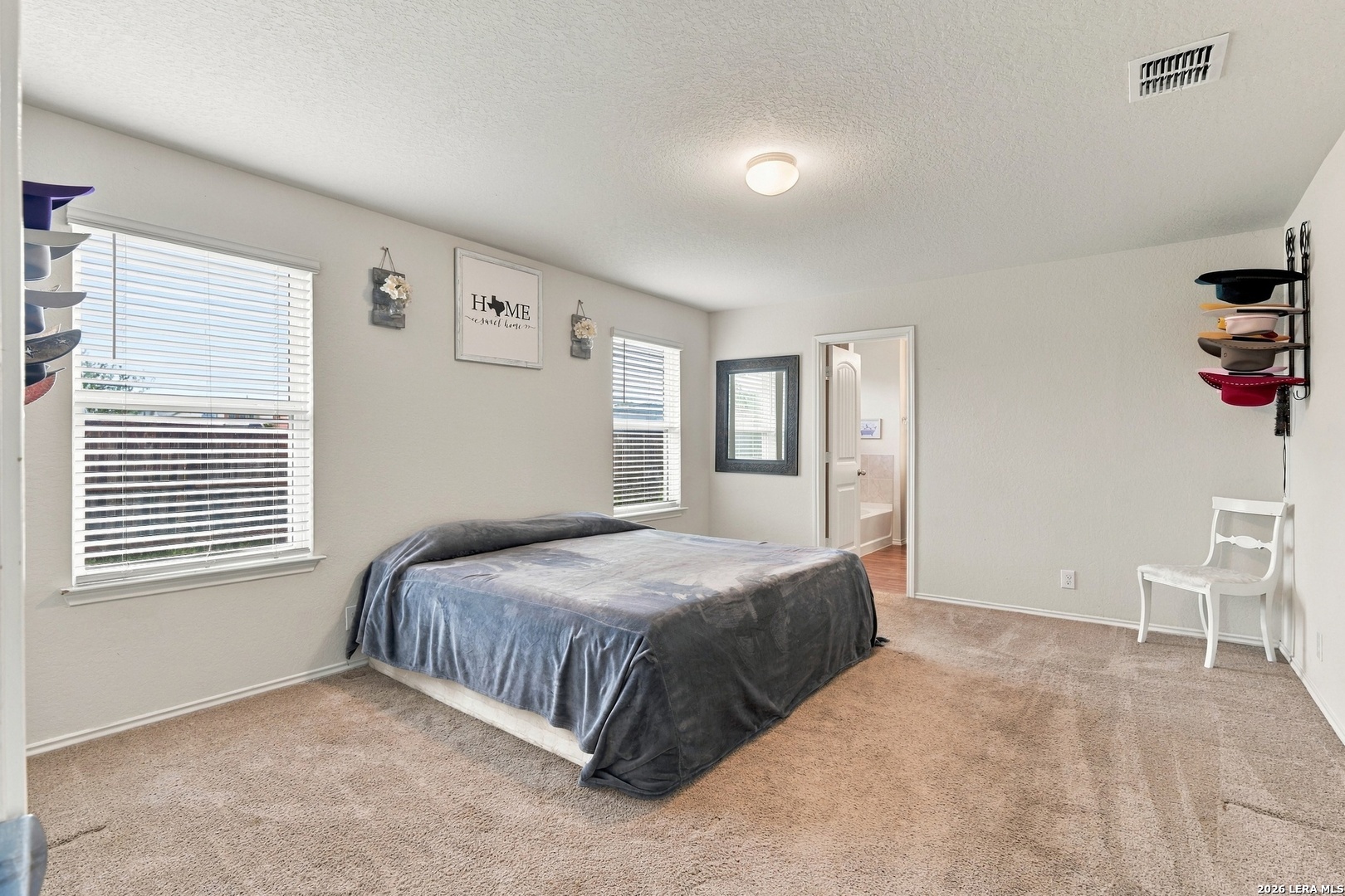 Carpeted bedroom with a gray-covered bed, two windows, and a bathroom doorway.
