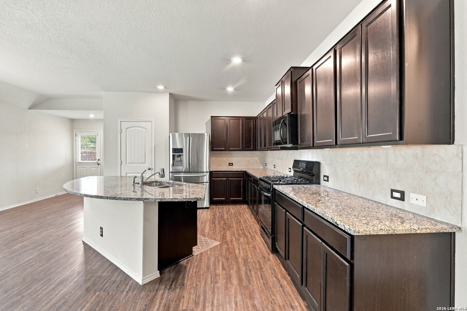 Vacant kitchen with dark wood cabinets, granite counters, a central island, and stainless steel appliances.