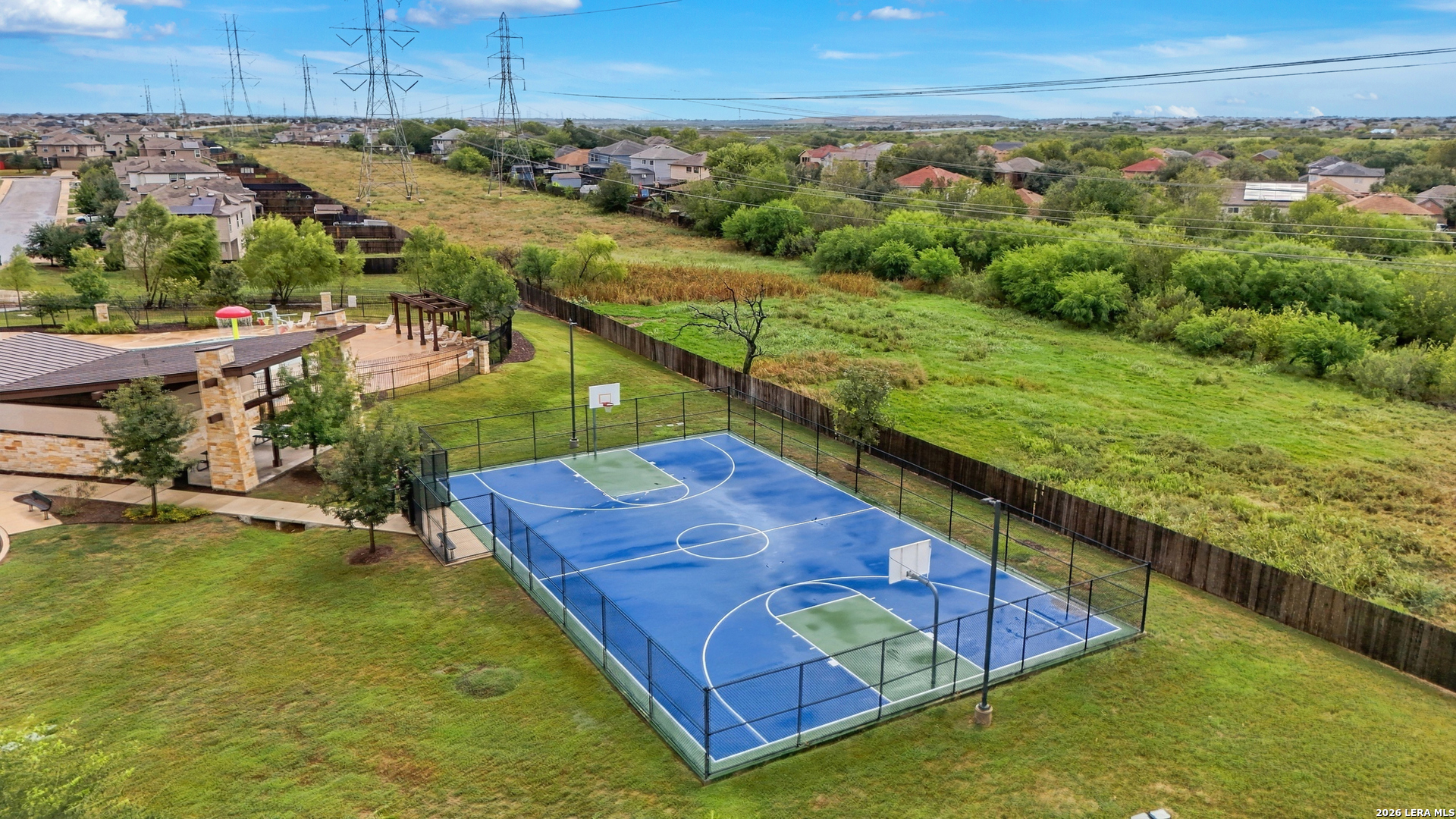Aerial view of a fenced basketball court beside a covered pavilion and pool.