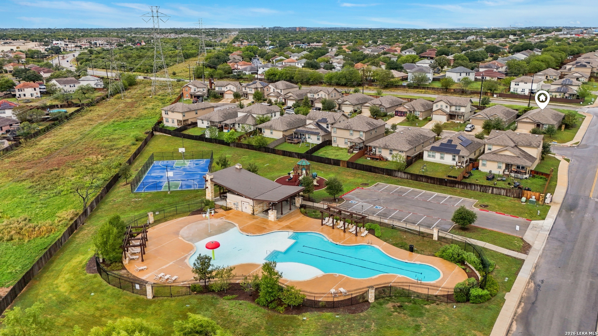Aerial view of a community pool, basketball court, playground, and pavilion among surrounding homes.