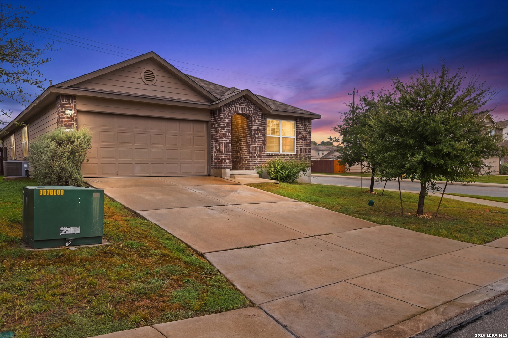 Single-story home with a wide garage and brick entry, photographed beneath a vivid dusk sky.