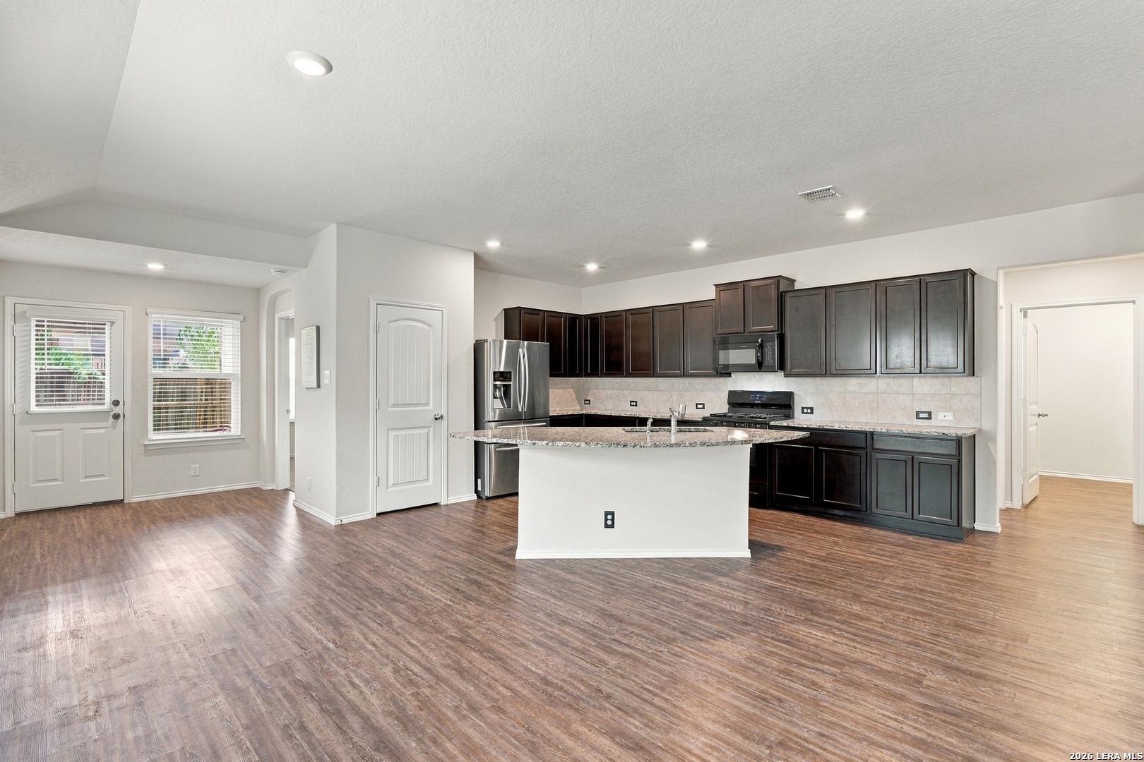 Kitchen with dark cabinets, granite island, stainless steel appliances, and wood-look floors.