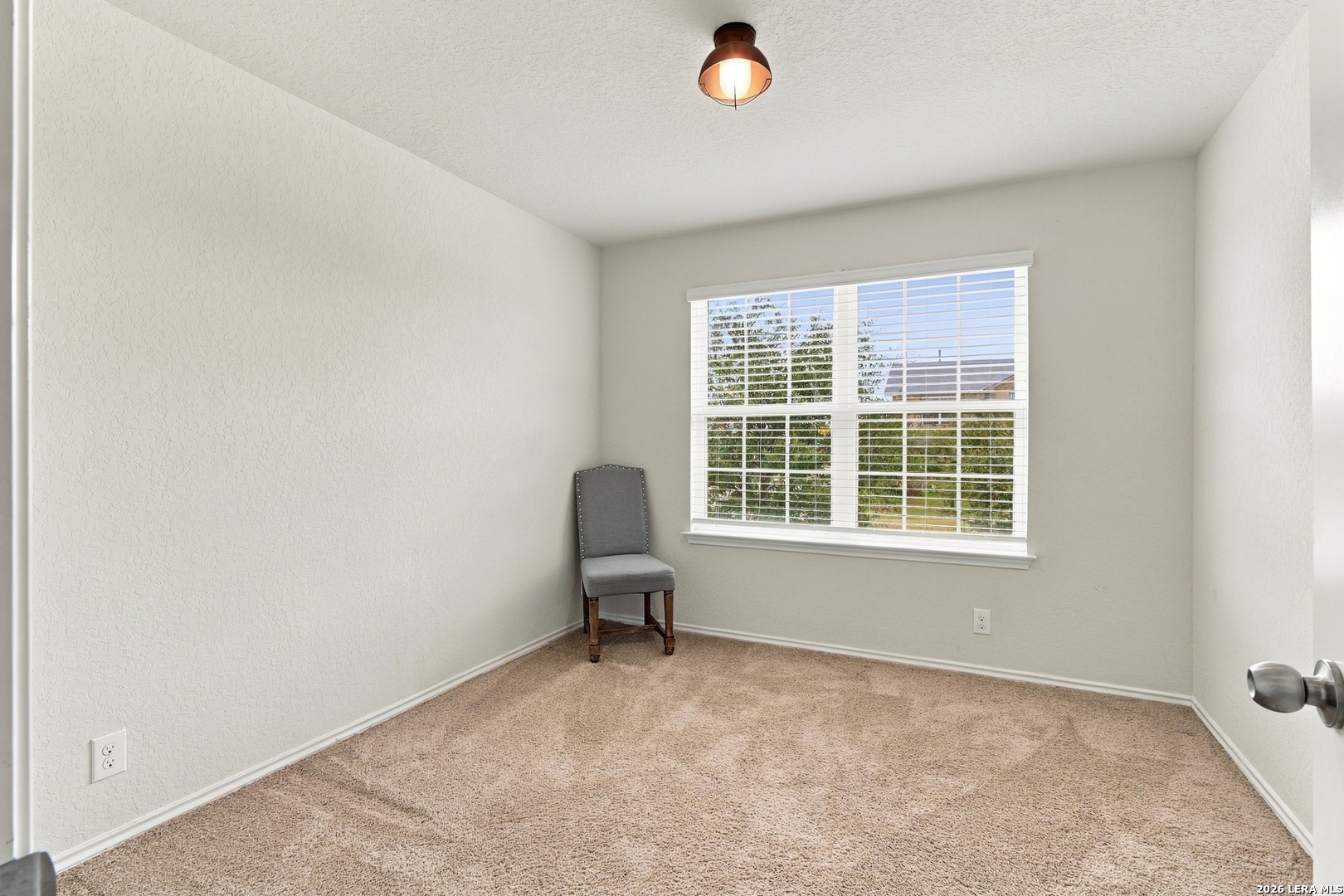 Carpeted room with a gray chair beside a large window with white blinds.
