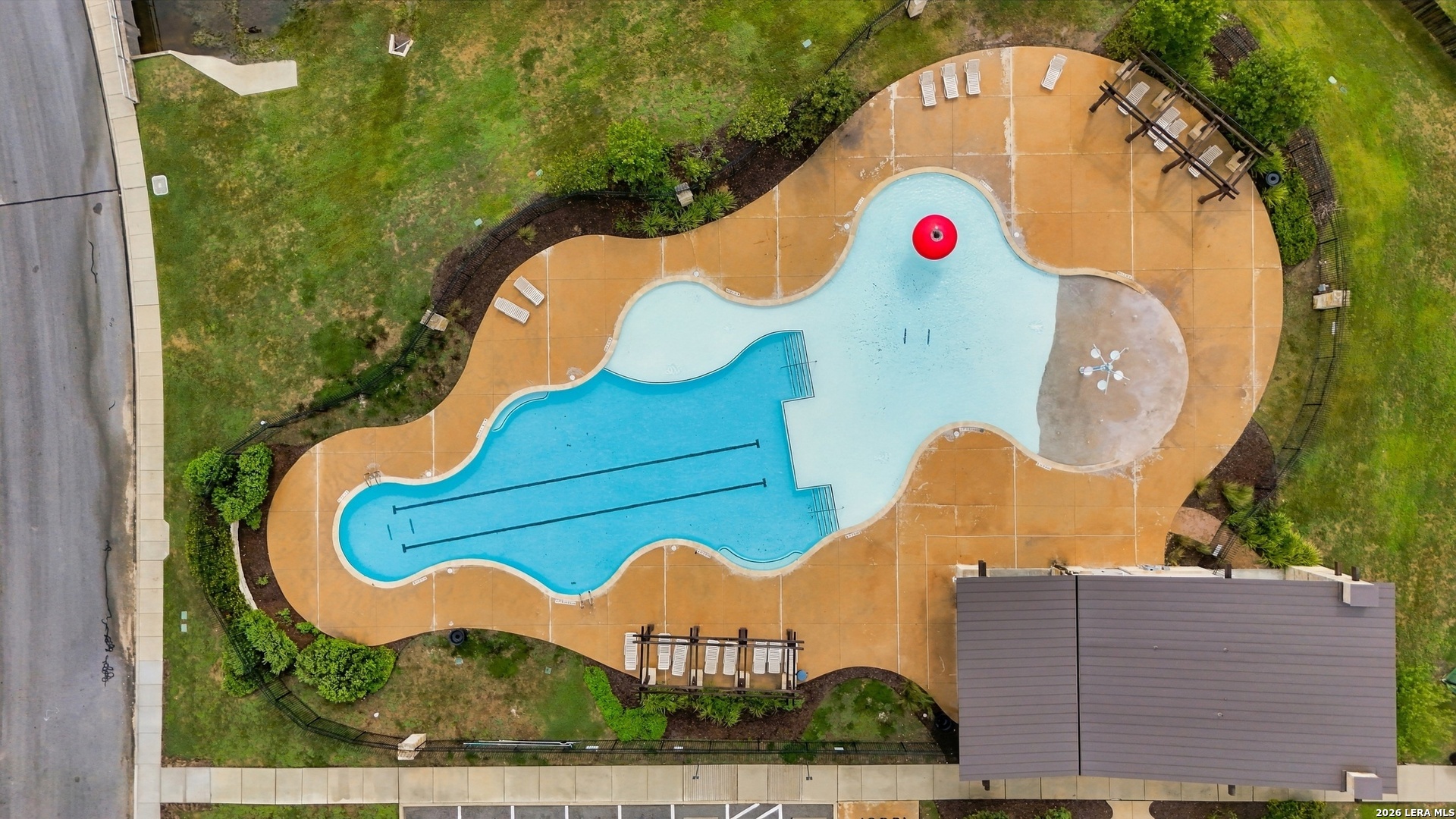 Aerial view of a freeform pool with a tan deck, lounge chairs, and a red floating ring.