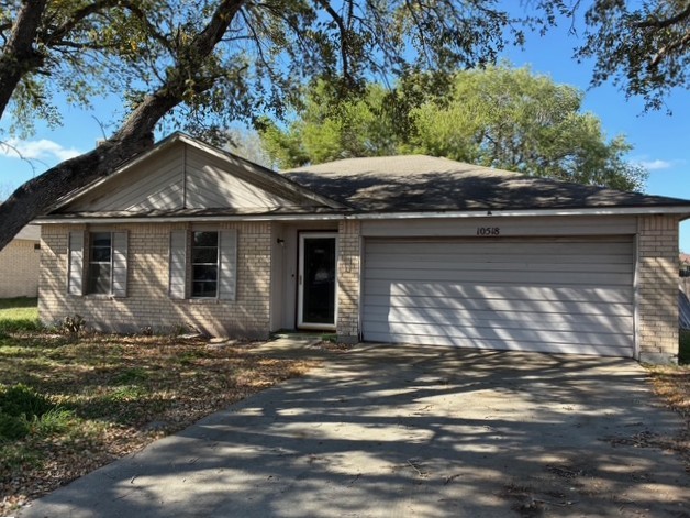 Single-story brick home with a two-car garage beneath mature shade trees.