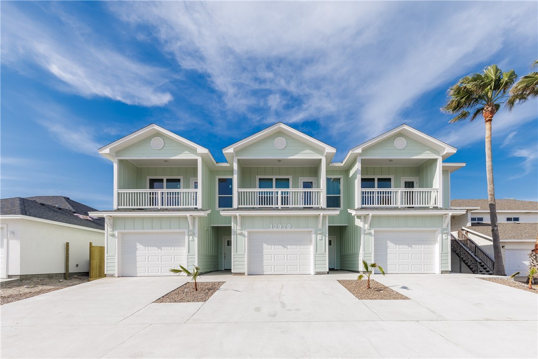 Three pale-green attached homes with upper balconies, white garage doors, and a palm tree.