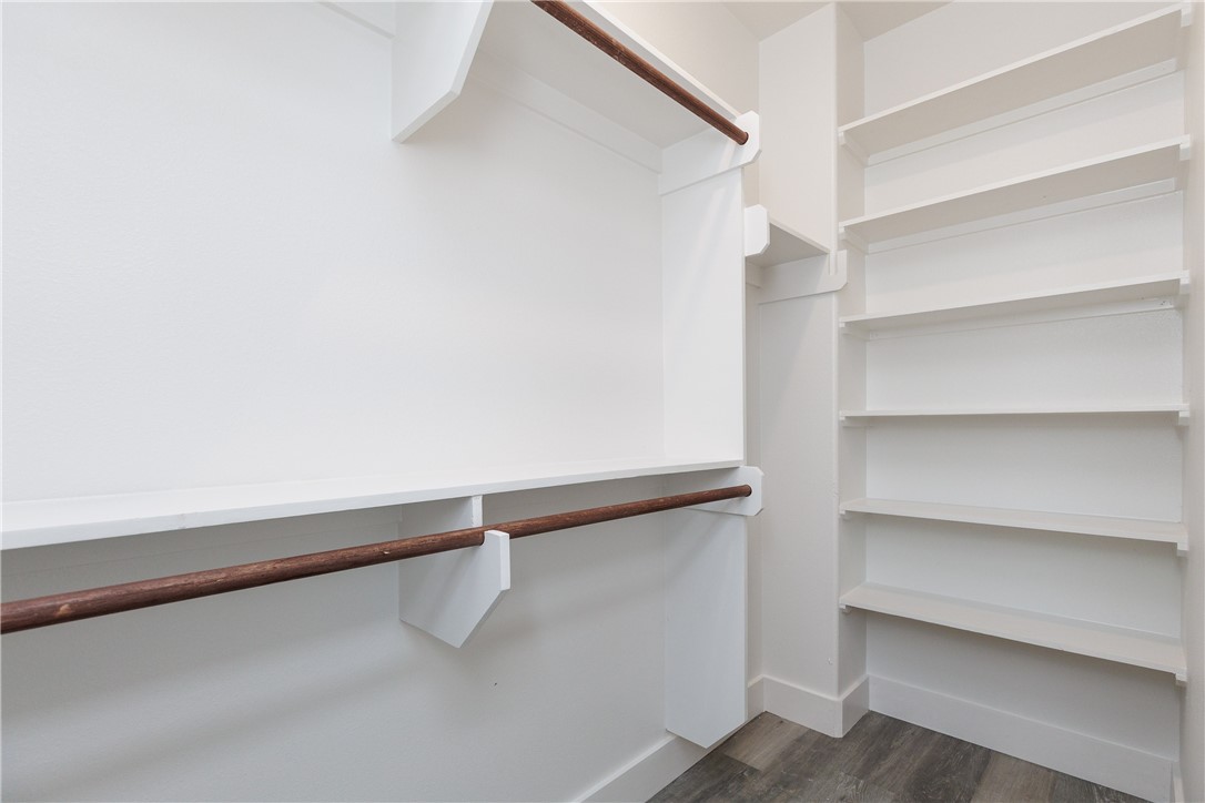 Walk-in closet with built-in white shelving, dark wood hanging rods, and wood-look flooring.