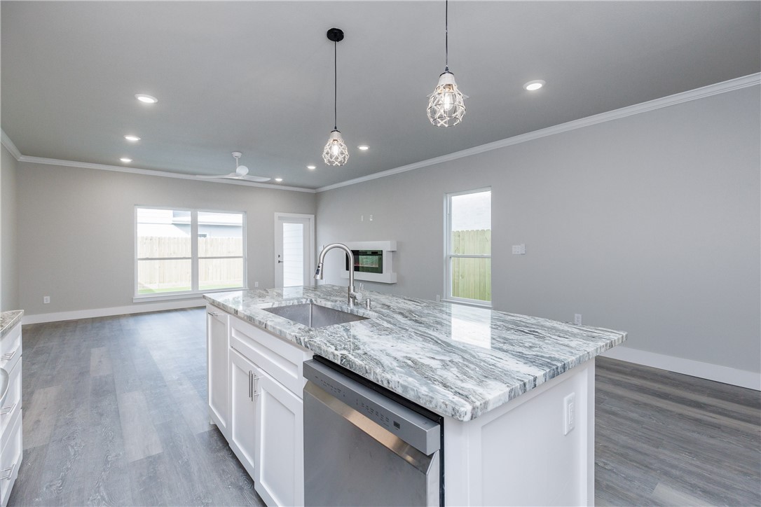 Kitchen with a large veined stone island, stainless dishwasher, and pendant lighting.