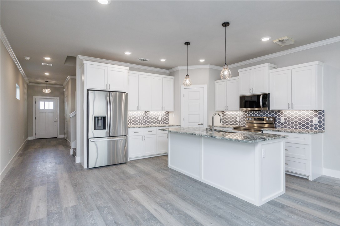 Vacant kitchen with white cabinets, stainless steel appliances, hexagonal backsplash, and a large stone-topped island.