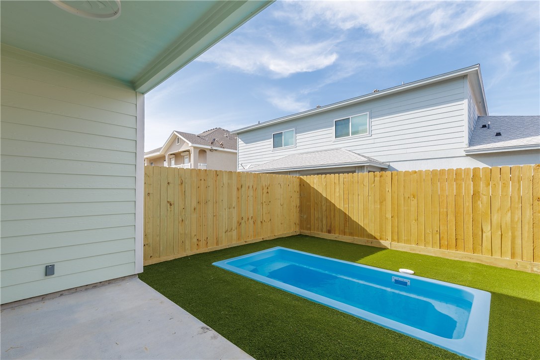 Backyard pool with artificial turf, wooden privacy fence, and covered patio.