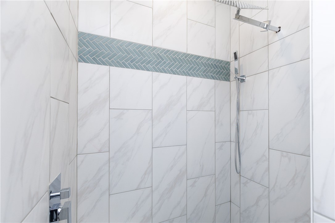Walk-in shower with a blue-gray herringbone tile accent and chrome rainfall showerhead.