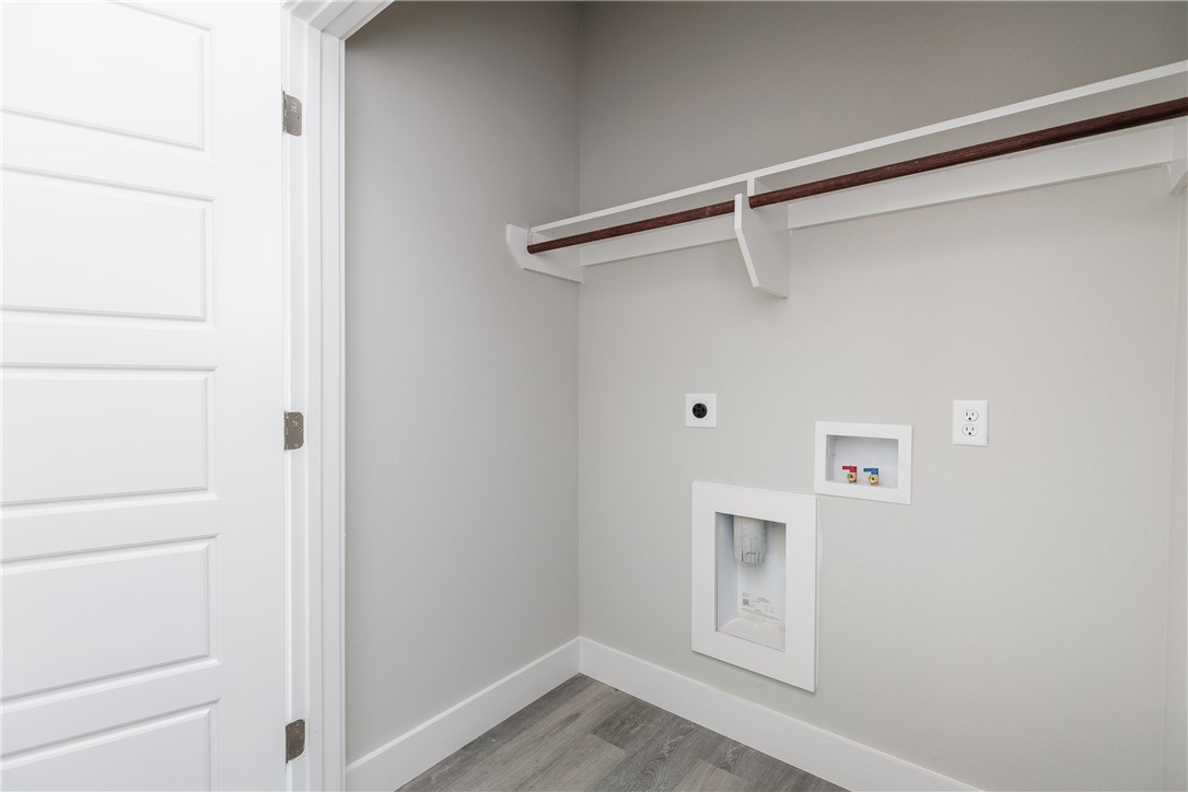 Empty laundry closet with washer and dryer hookups and a shelf with hanging rod.