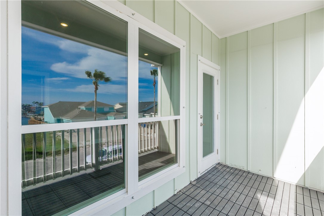 Covered balcony with pale green siding, dark tile flooring, and windows reflecting palm trees.