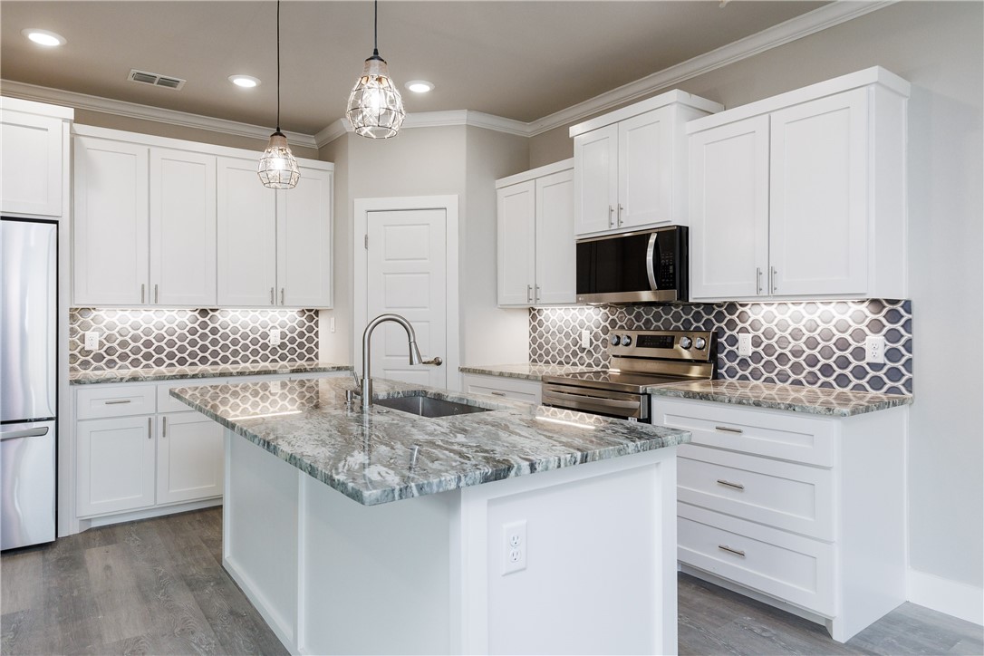 Kitchen with white cabinets, a stone island, stainless steel appliances, and a geometric backsplash.