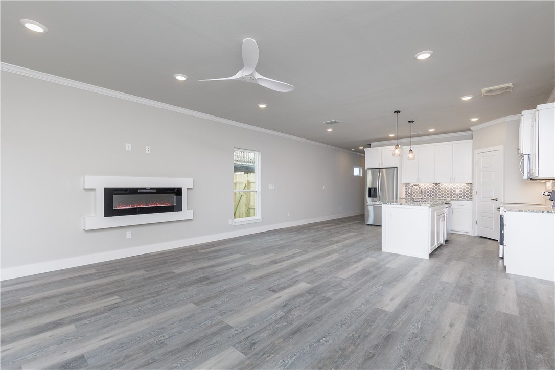 Open-plan living room and kitchen with gray plank floors, white cabinetry, and a wall-mounted electric fireplace.