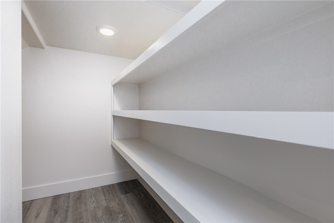 Walk-in closet with long white built-in shelves and dark wood-look flooring.